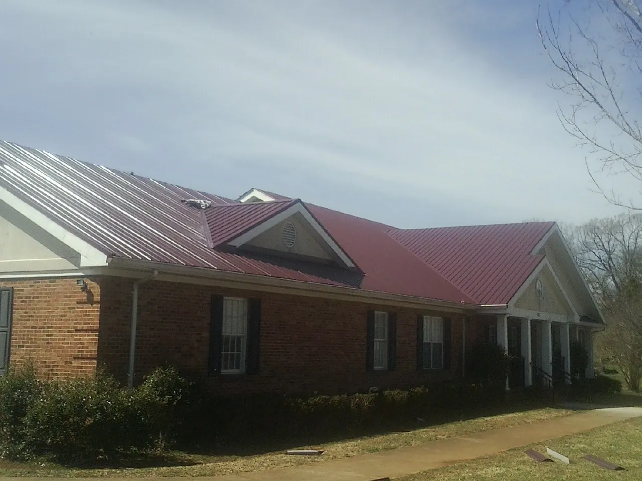 Red metal roof with gabled entries on a long brick building, from a Hail Damage Roof Repair job in Black River