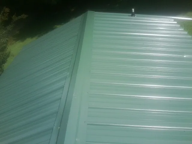 New green metal panels meeting at the ridge of a roof — Flat Roof Repair work by our crew in Black River