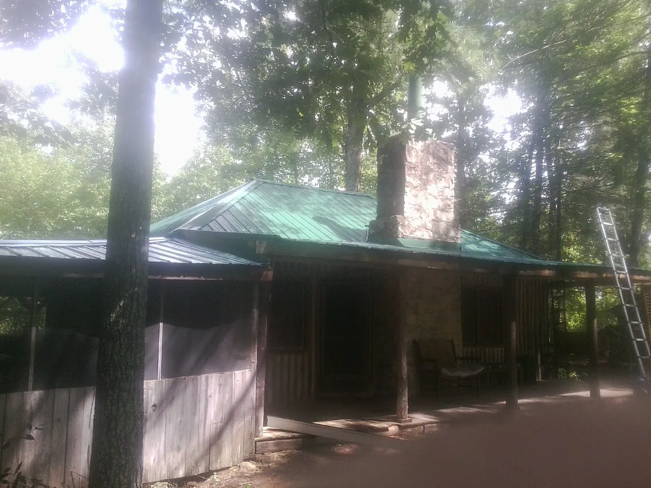 Green metal roof and stone chimney above a log cabin porch in Black River