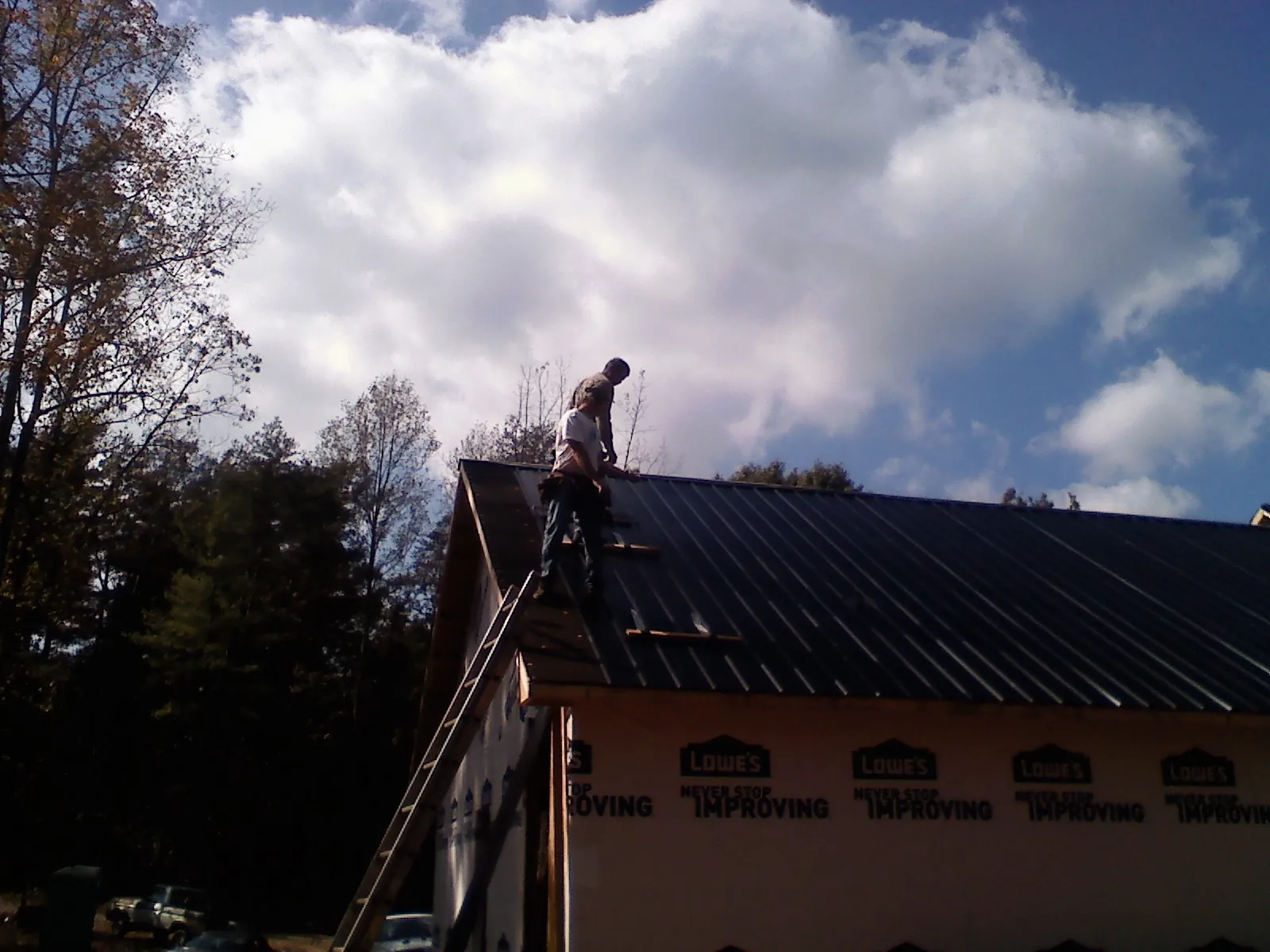Roofer fastening dark metal panels high against a cloudy sky, from a Roof Inspection job in Black River